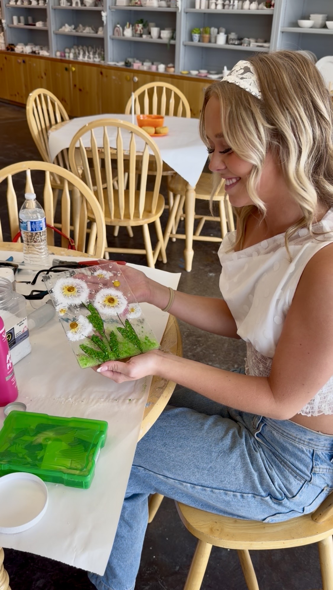 A smiling guest holding her fused glass daisy panel at Paint Fusion in Park City