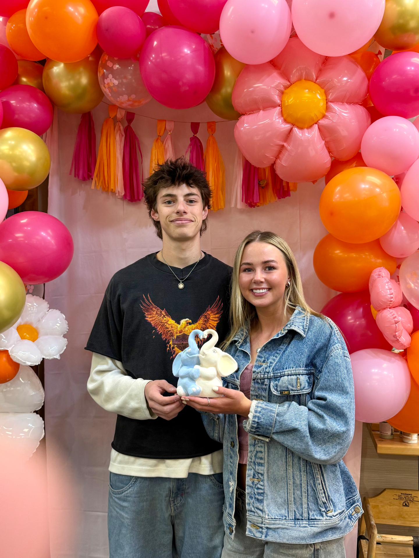 A couple holding their elephant pottery under a balloon arch at a studio event
