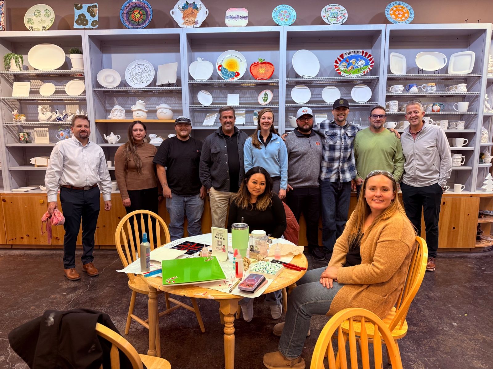 A corporate group smiling around a table with their projects at Paint Fusion Park City