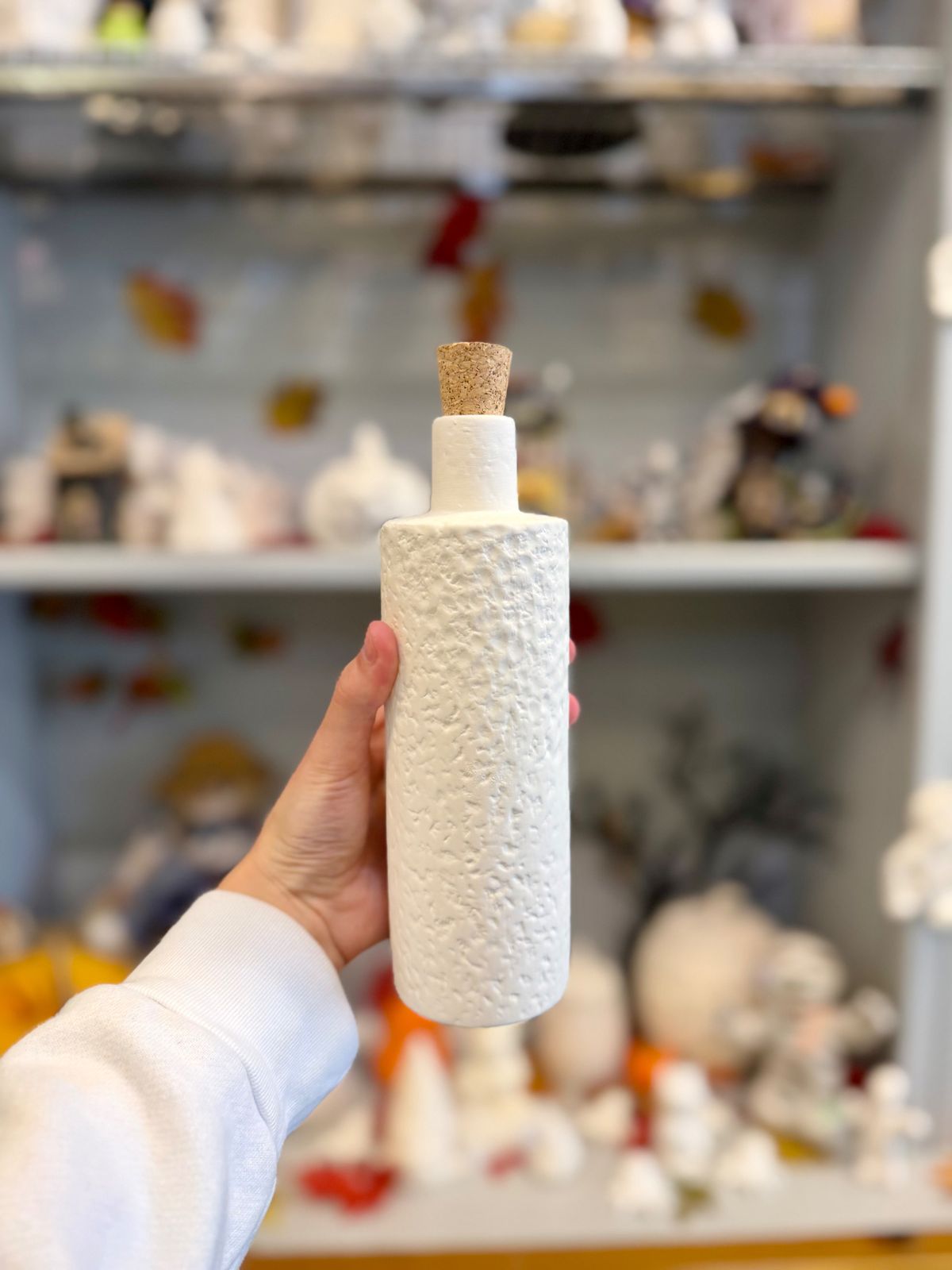 A hand holding a textured white pottery bottle with a cork stopper from the Paint Fusion Park City store