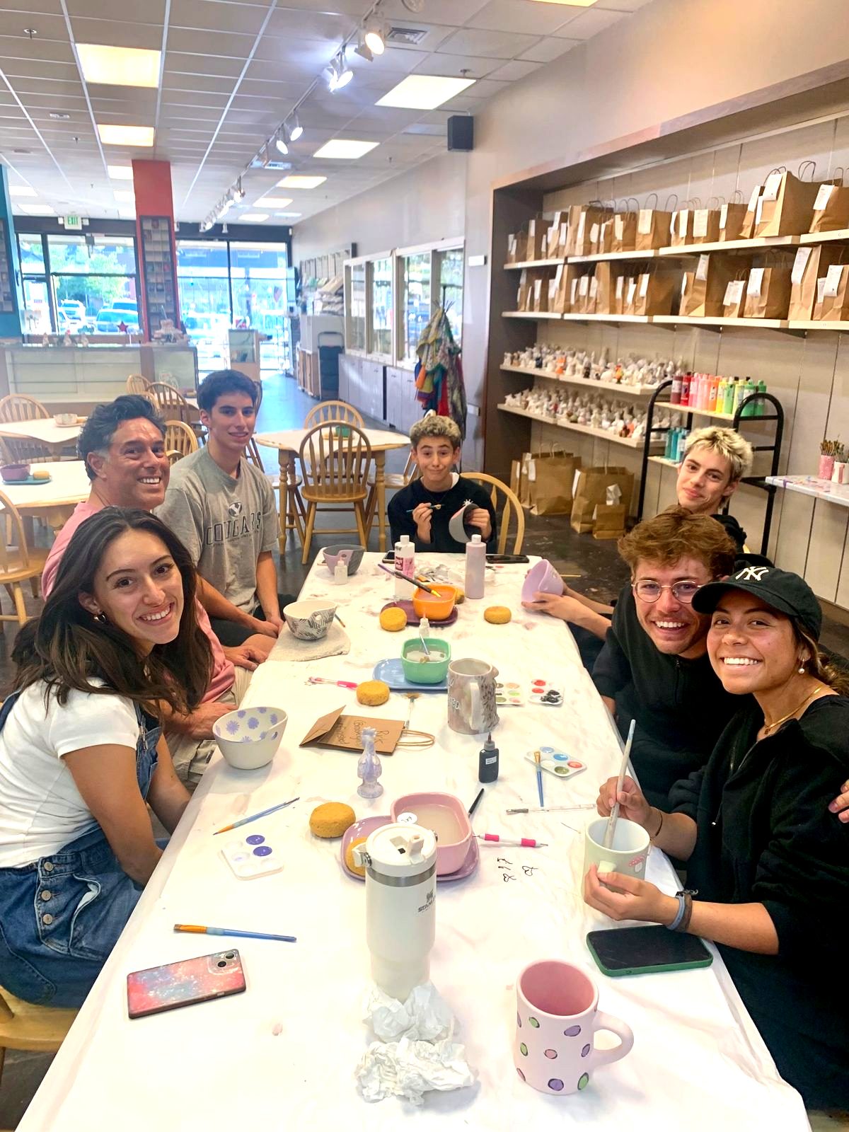 A group smiling around a table full of pottery painting at Paint Fusion Park City